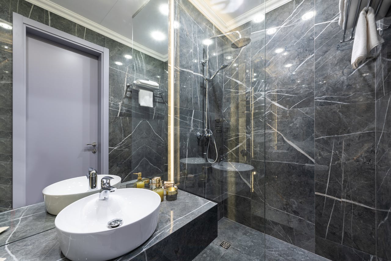 Shower cabin against washbasin and assorted hygiene products reflecting in mirror under luminous lamps at home